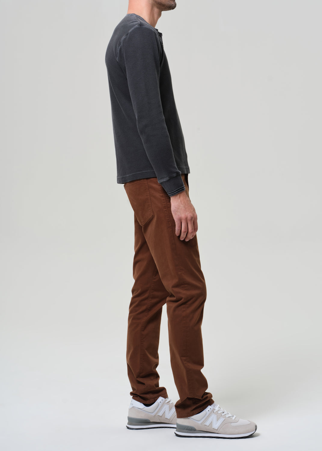 Person wearing a grey long-sleeve shirt and brown pants on a grey background