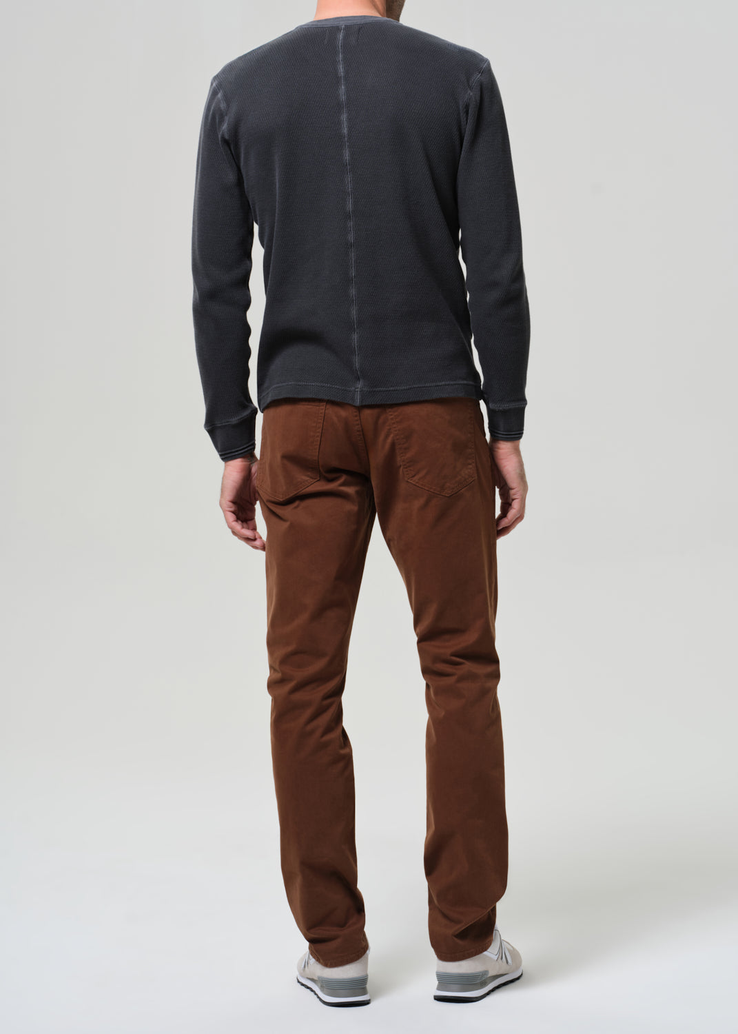 Person wearing a grey long-sleeve shirt and brown pants on a grey background