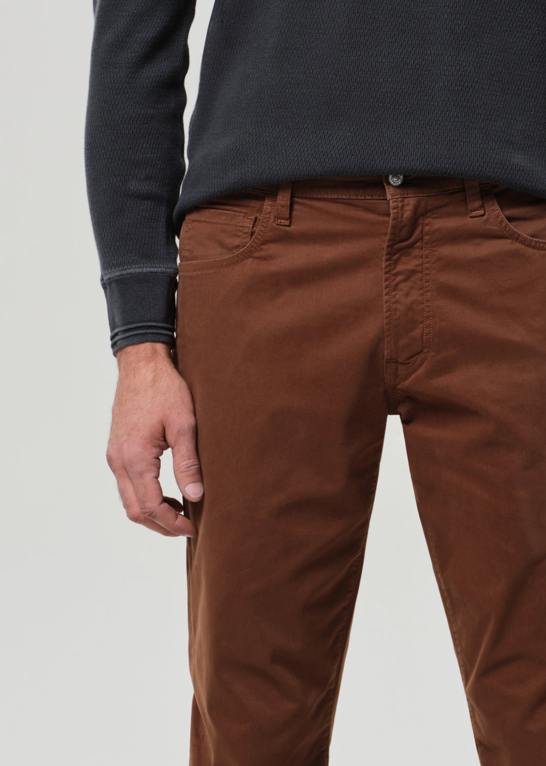 Person wearing a grey long-sleeve shirt and brown pants on a grey background