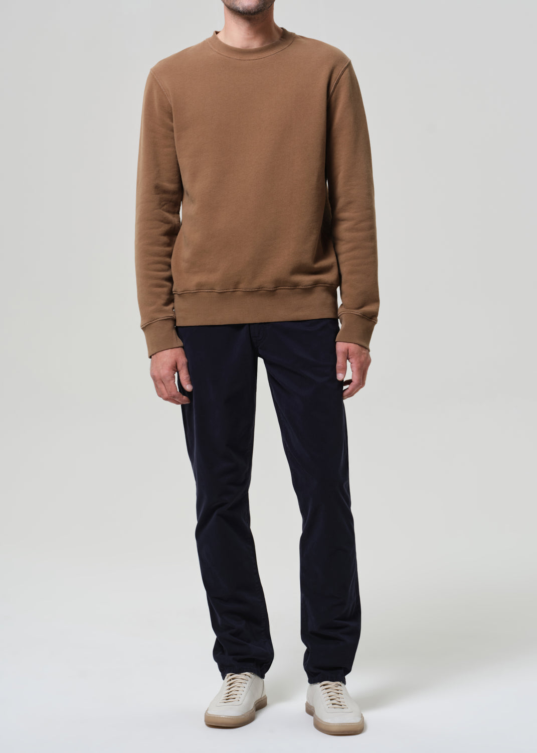 Person wearing a brown sweatshirt and black pants on a white background