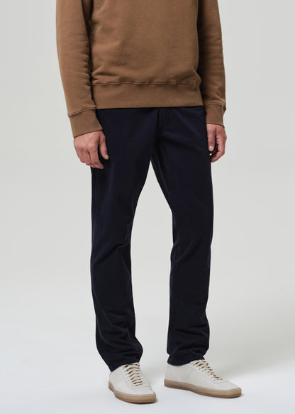 Person wearing a brown sweatshirt and black pants with white shoes on a plain background