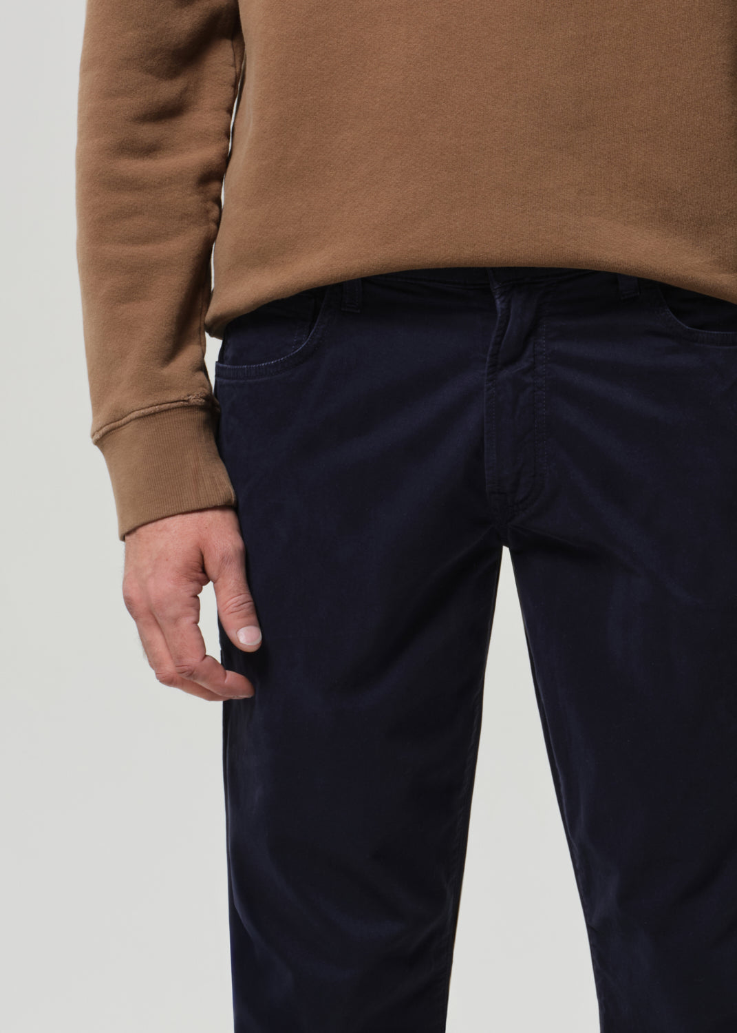 Person wearing a brown sweater and dark blue pants on a plain background