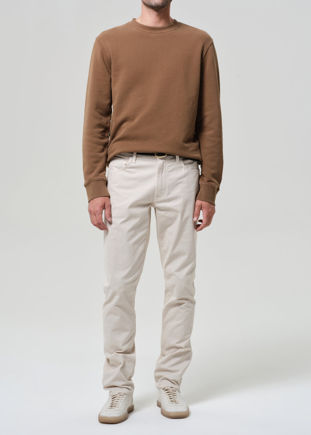 Person wearing a brown sweater and light taupe pants on a plain background
