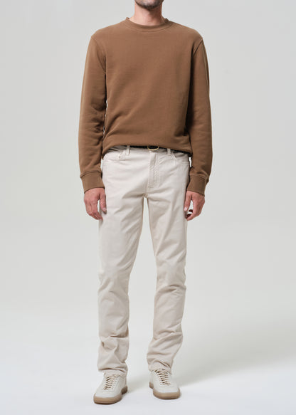 Person wearing a brown sweater and light taupe pants on a plain background