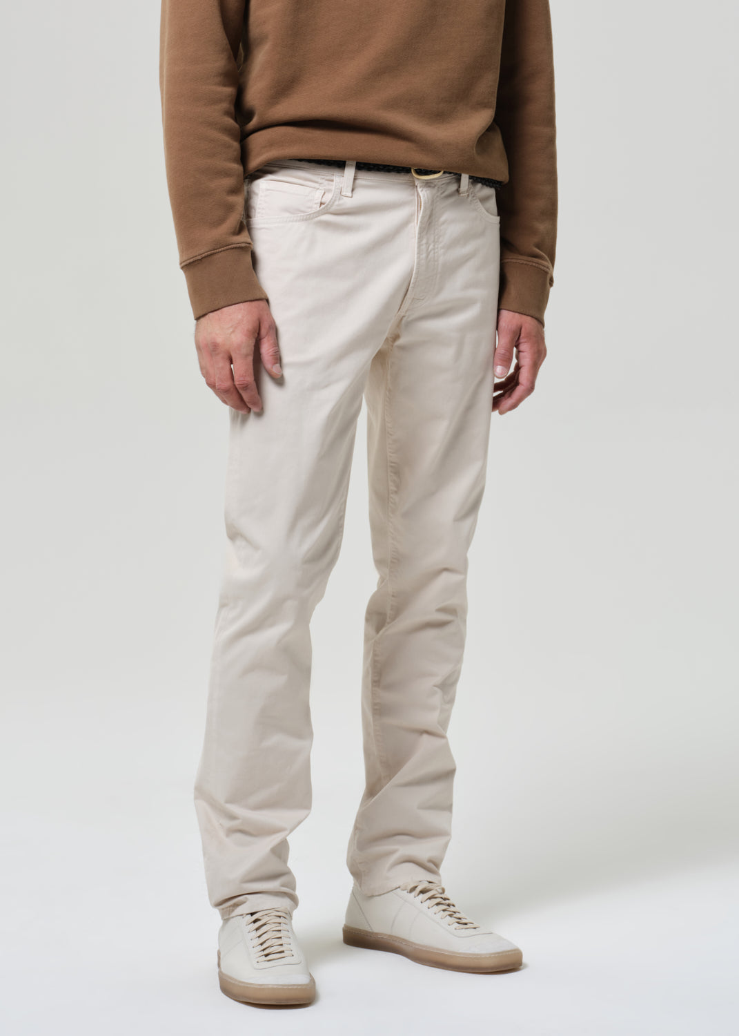 Person wearing a brown sweater and light taupe pants on a plain background