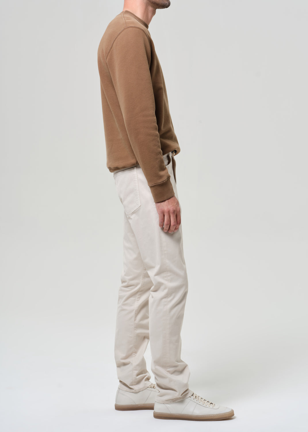 Person wearing a brown sweater and light taupe pants on a plain background
