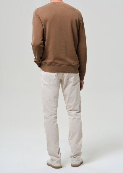 Person wearing a brown sweater and light taupe pants on a plain background