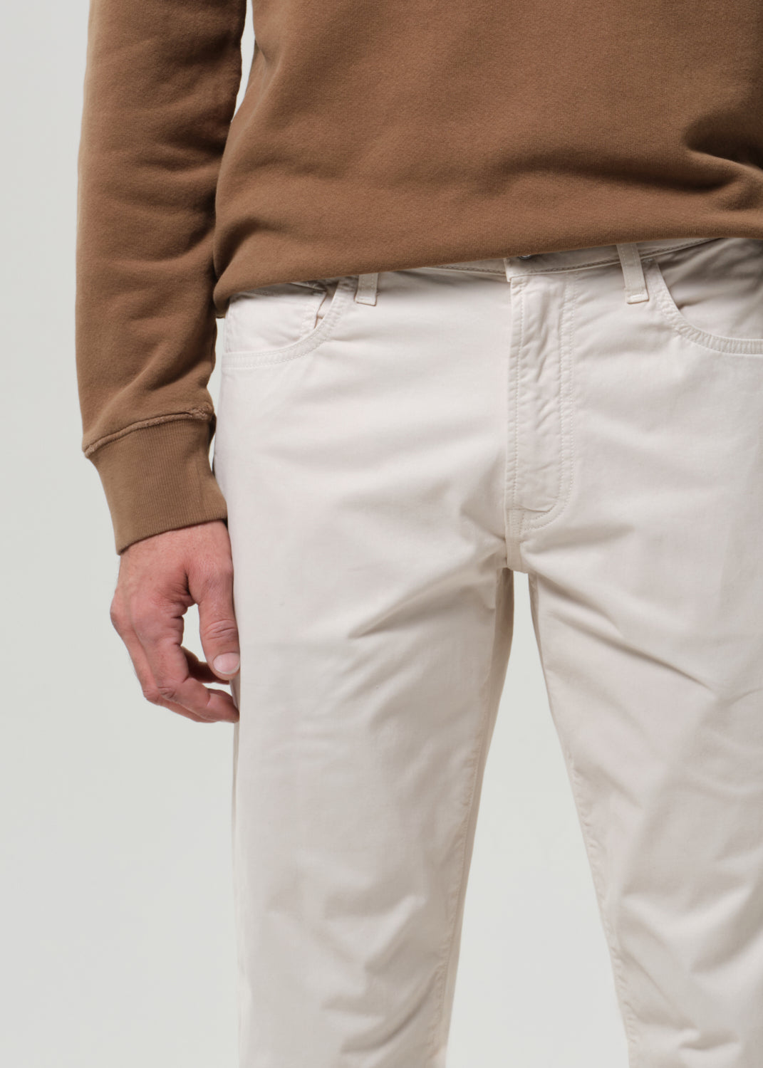 Person wearing a brown sweater and light taupe pants on a plain background