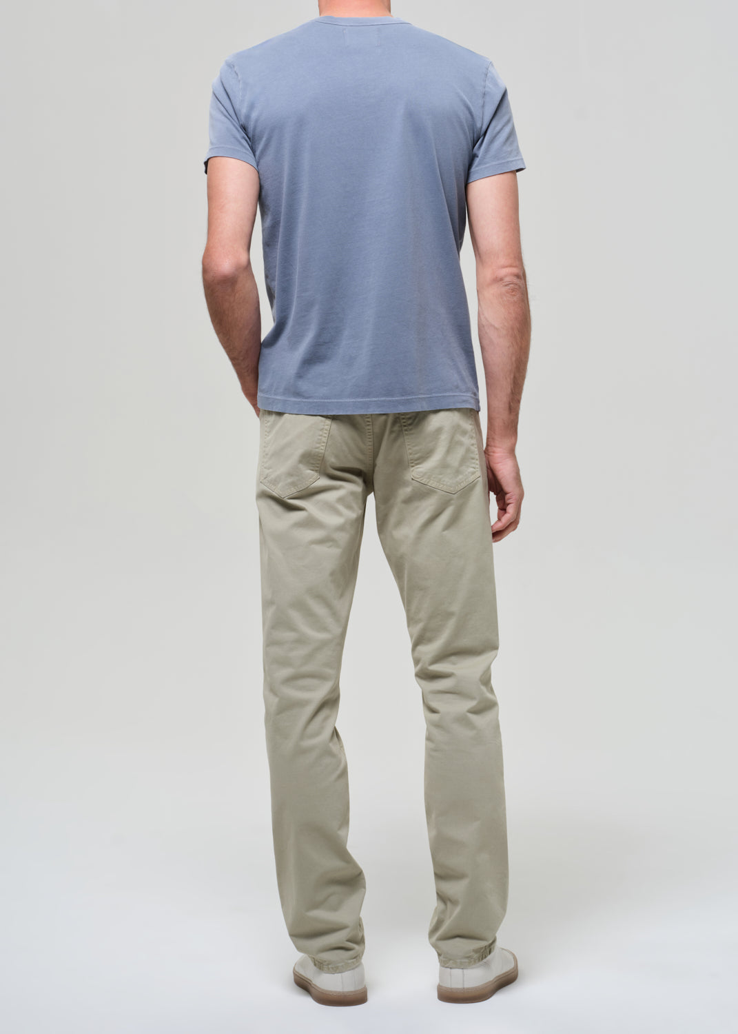 Person wearing a light blue t-shirt and light green pants on a grey background