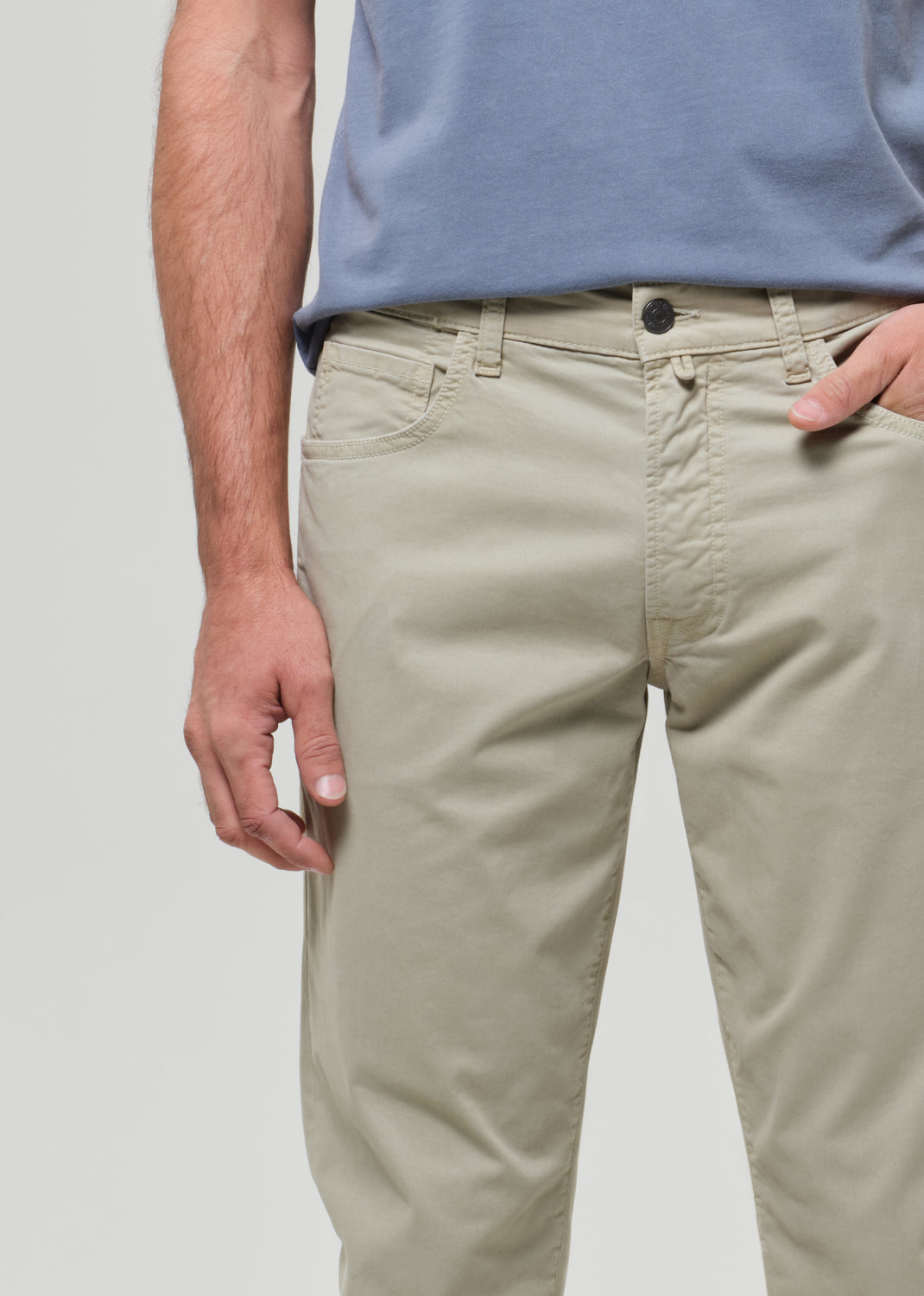 Person wearing a light blue t-shirt and light green pants on a grey background