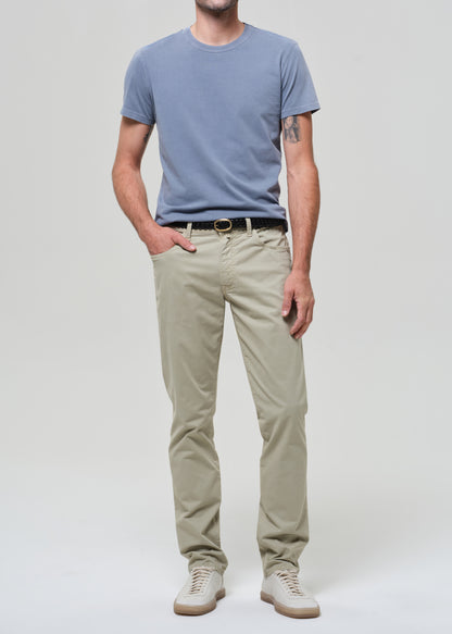 Person wearing a light blue t-shirt and light green pants on a grey background