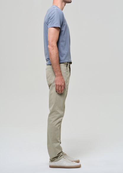 Person wearing a light blue t-shirt and light green pants on a grey background