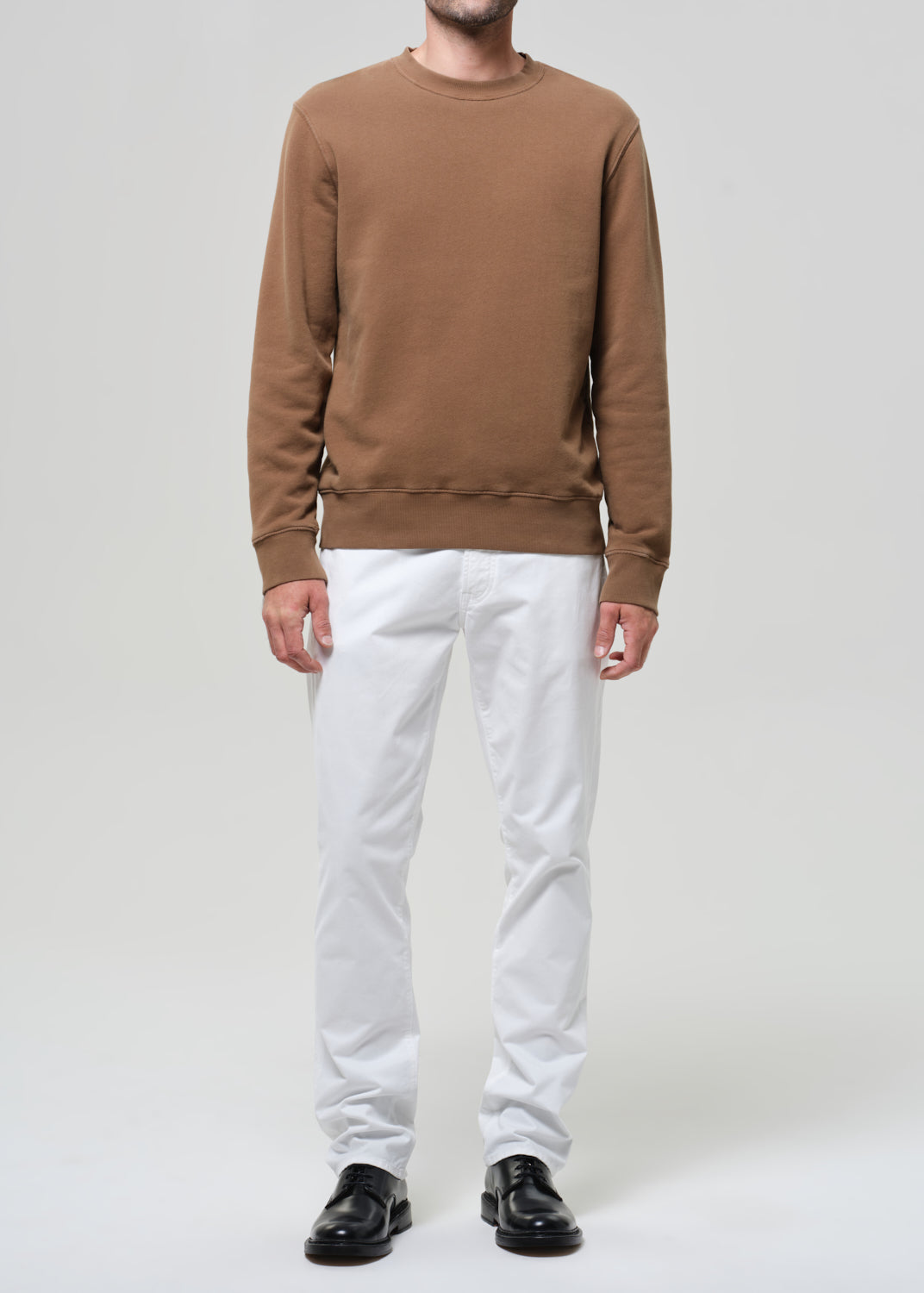 Person wearing a brown sweatshirt, white pants, and black shoes on a plain background