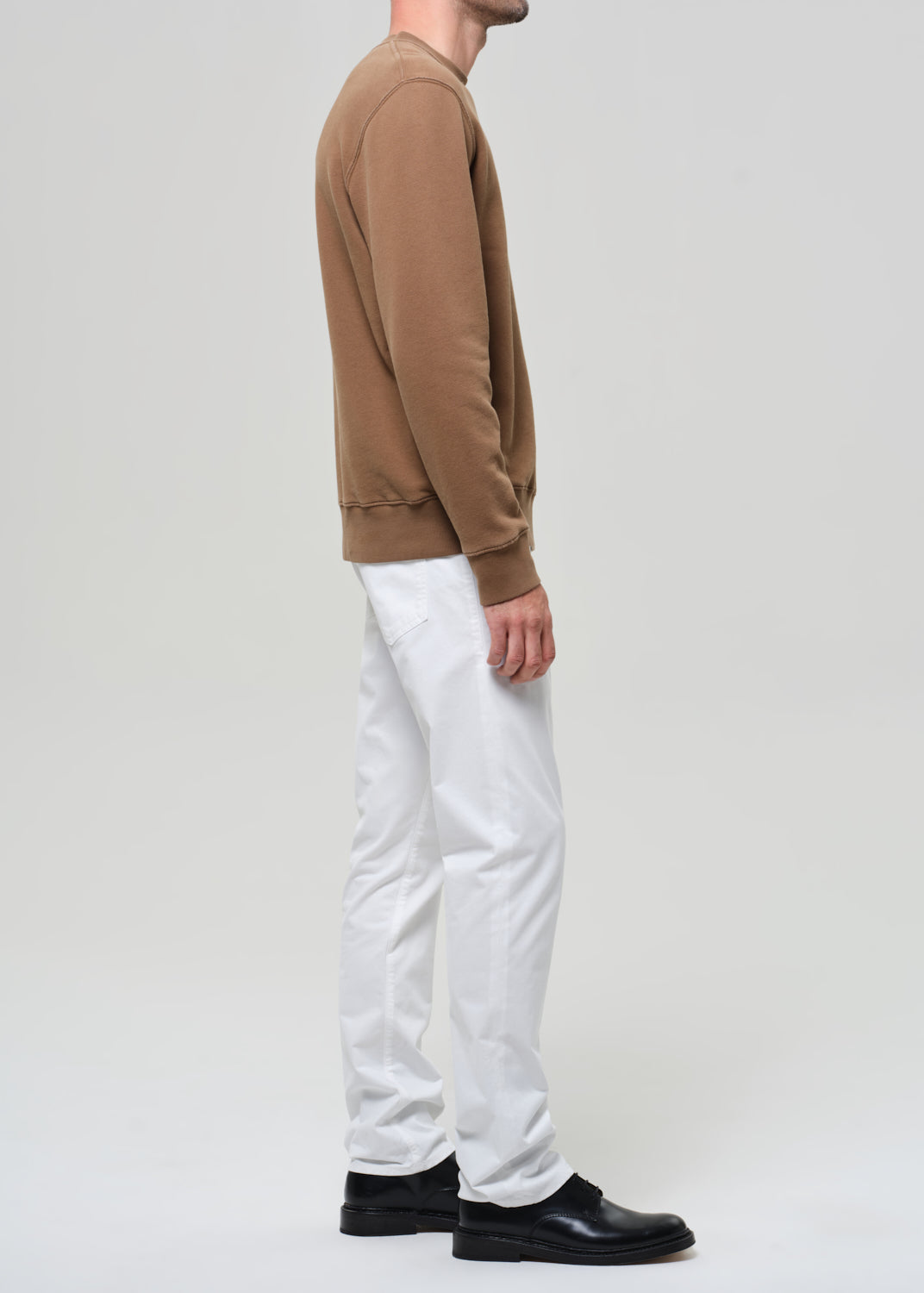 Person wearing a brown sweatshirt, white pants, and black shoes on a plain background