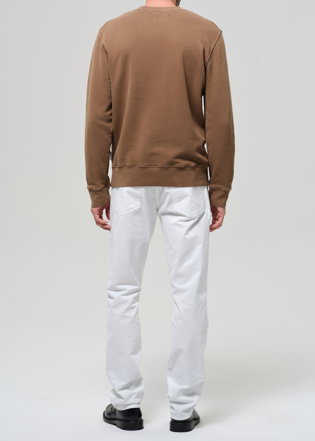 Person wearing a brown sweater and white pants on a plain background