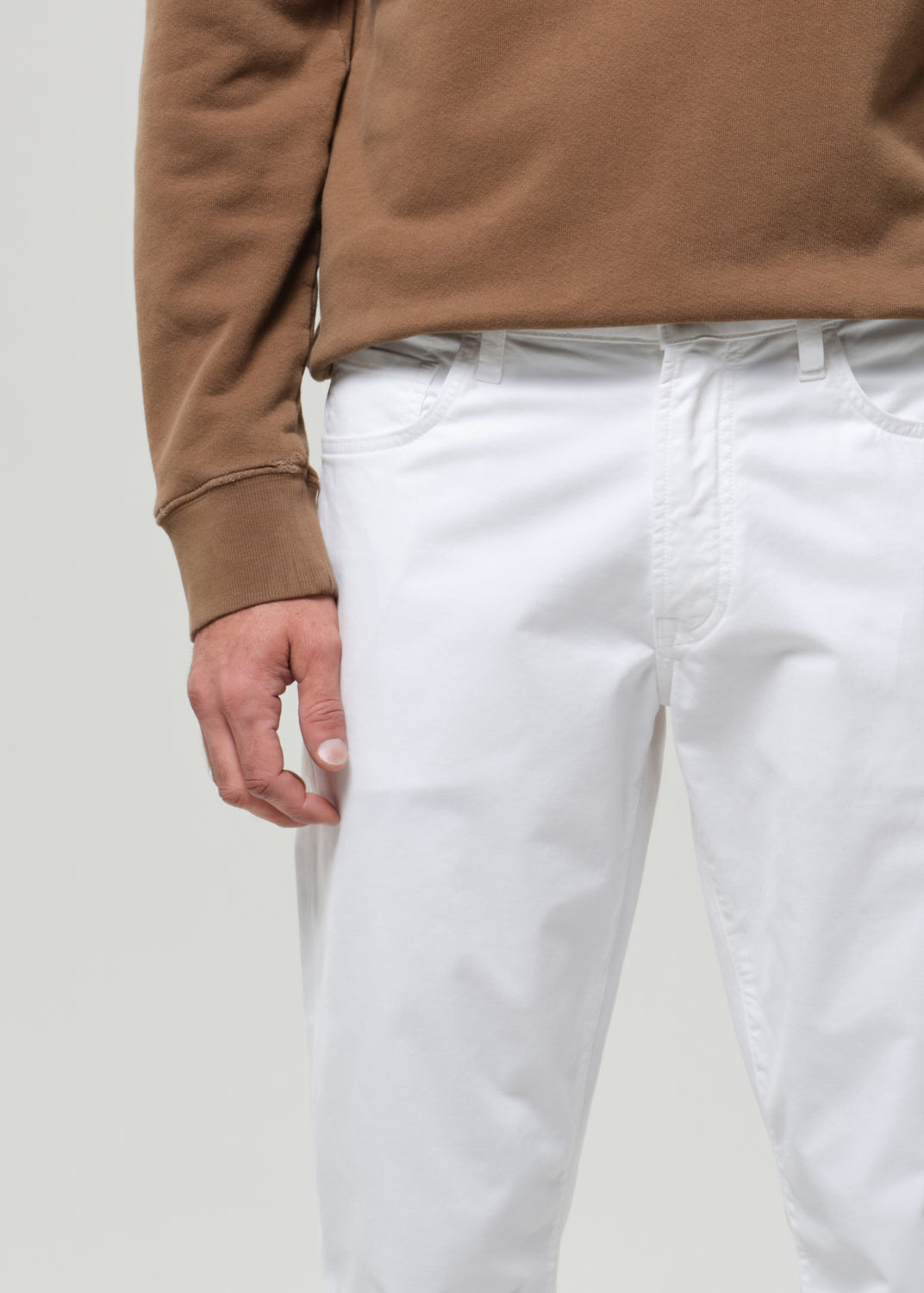 Person wearing a brown sweatshirt and white pants on a plain background