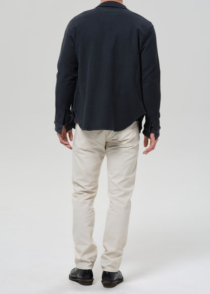 A man shown from the back wearing a dark navy long-sleeve button-up shirt, off-white chino pants, and black shoes, photographed against a grey background.