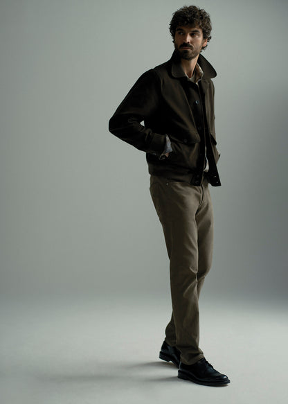 A man modeling a dark brown jacket, brown shirt, khaki trousers, and black leather shoes against a neutral gray studio background.