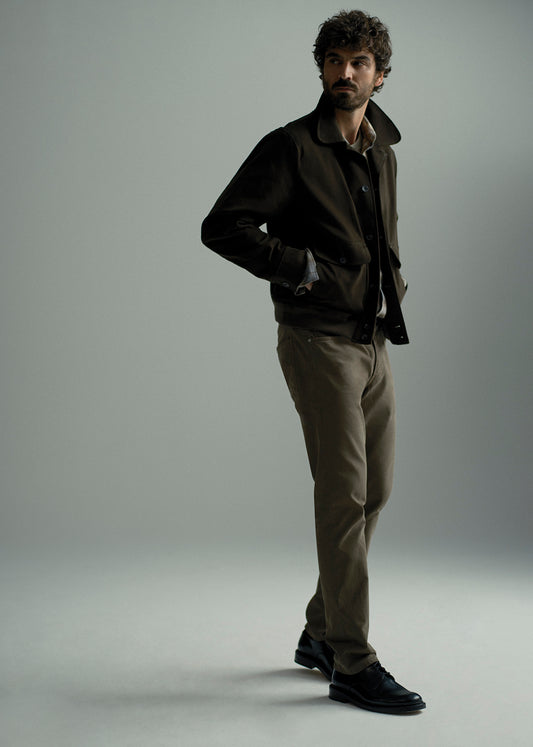 A man modeling a dark brown jacket, brown shirt, khaki trousers, and black leather shoes against a neutral gray studio background.