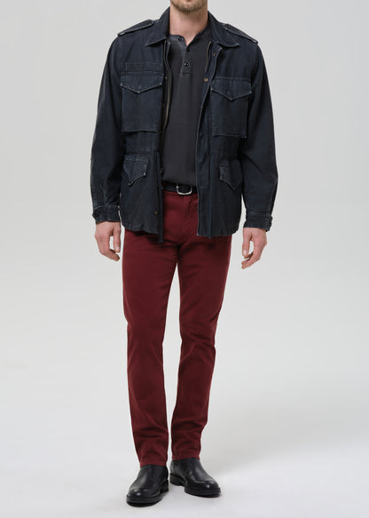 Person wearing a dark jacket, black shirt, red pants, and black shoes on a grey background