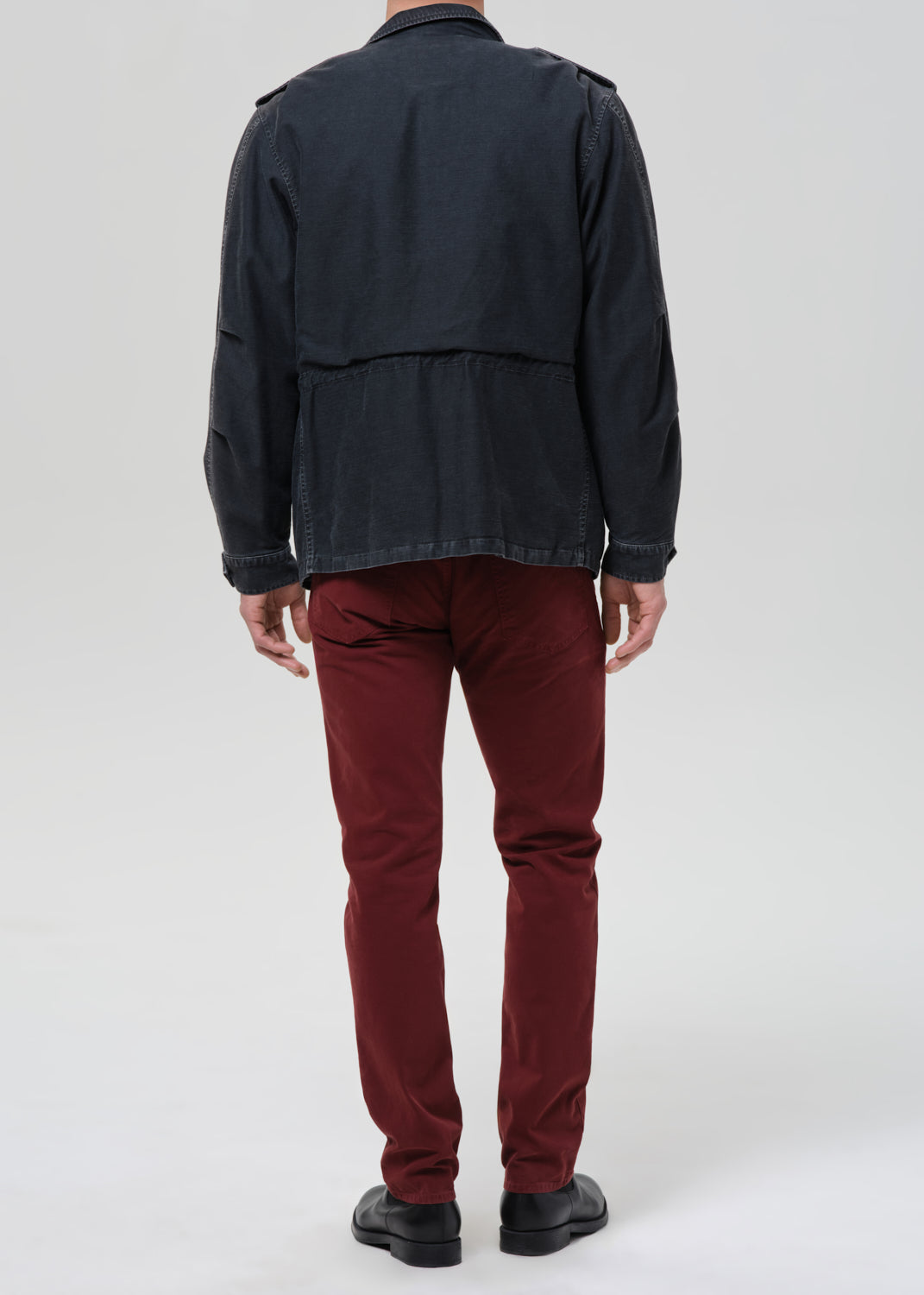 Person wearing a dark jacket and red pants on a grey background