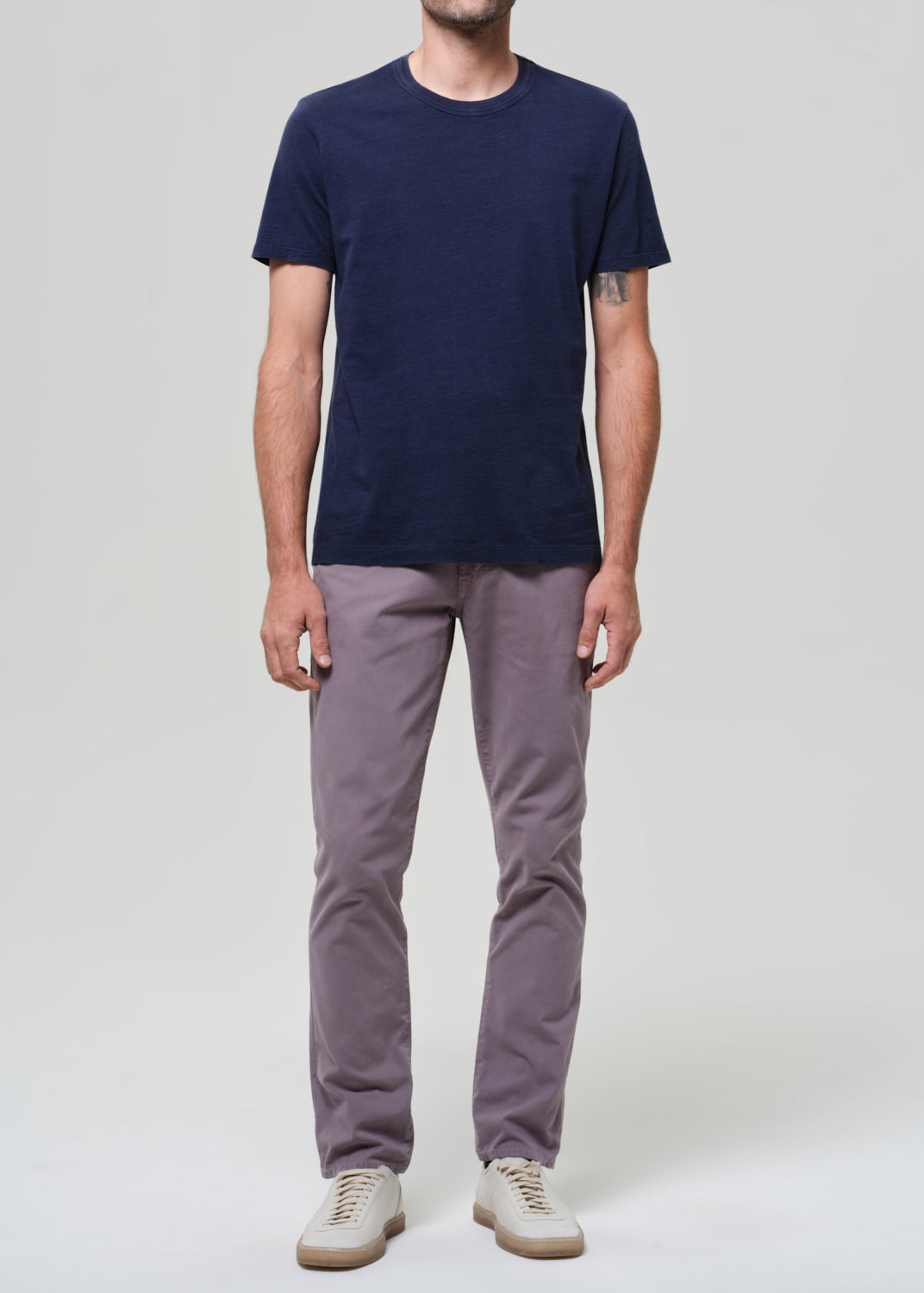 Person wearing a navy t-shirt and grey pants on a grey background