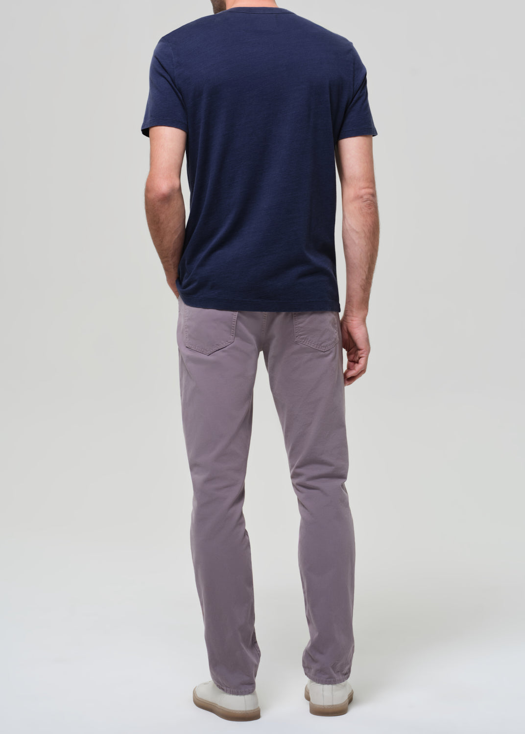 Person wearing a navy t-shirt and grey pants on a grey background