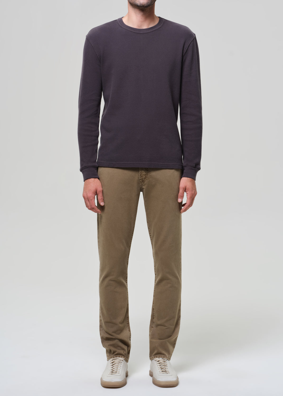 Person wearing a dark long-sleeve shirt and beige pants on a grey background