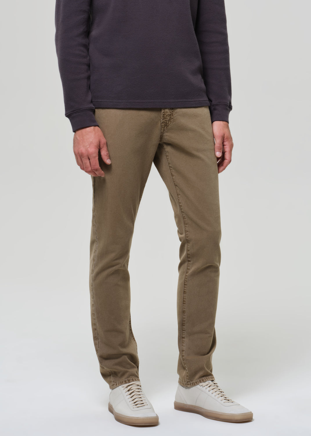 Person wearing a dark long-sleeve shirt and beige pants on a grey background