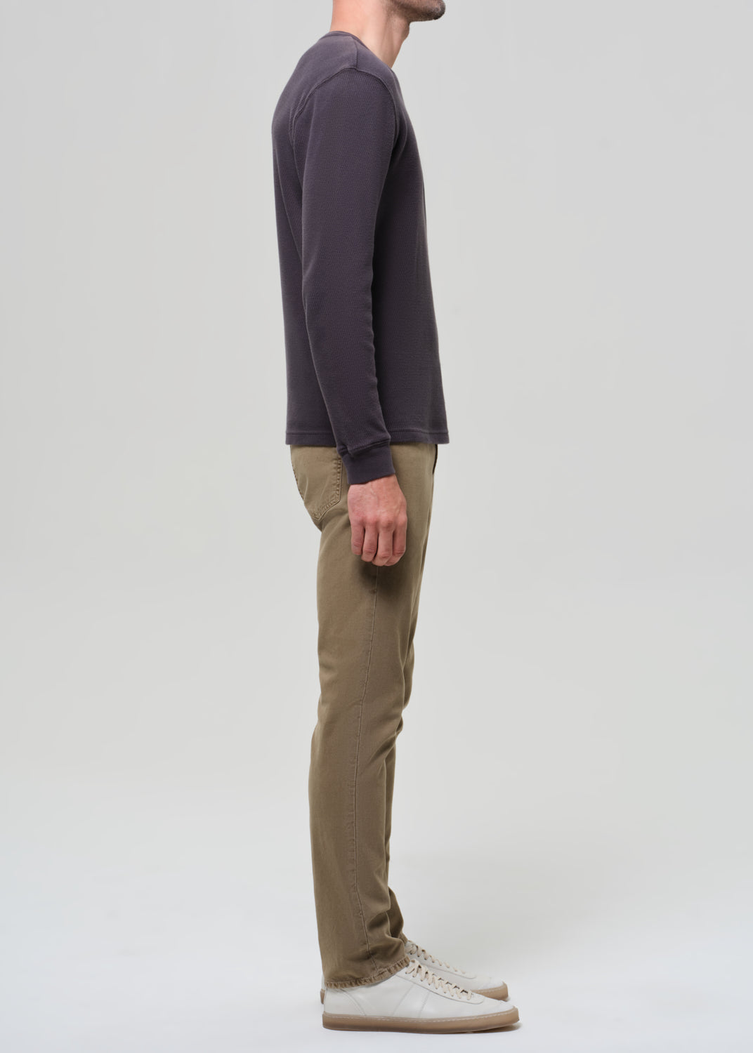 Person wearing a dark long-sleeve shirt and beige pants on a grey background