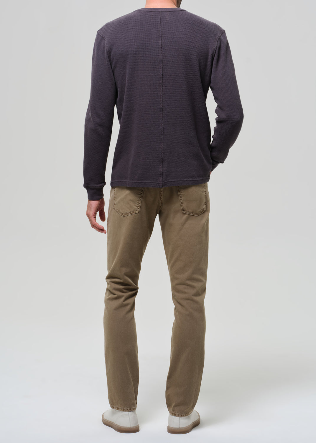 Person wearing a dark long-sleeve shirt and beige pants on a grey background