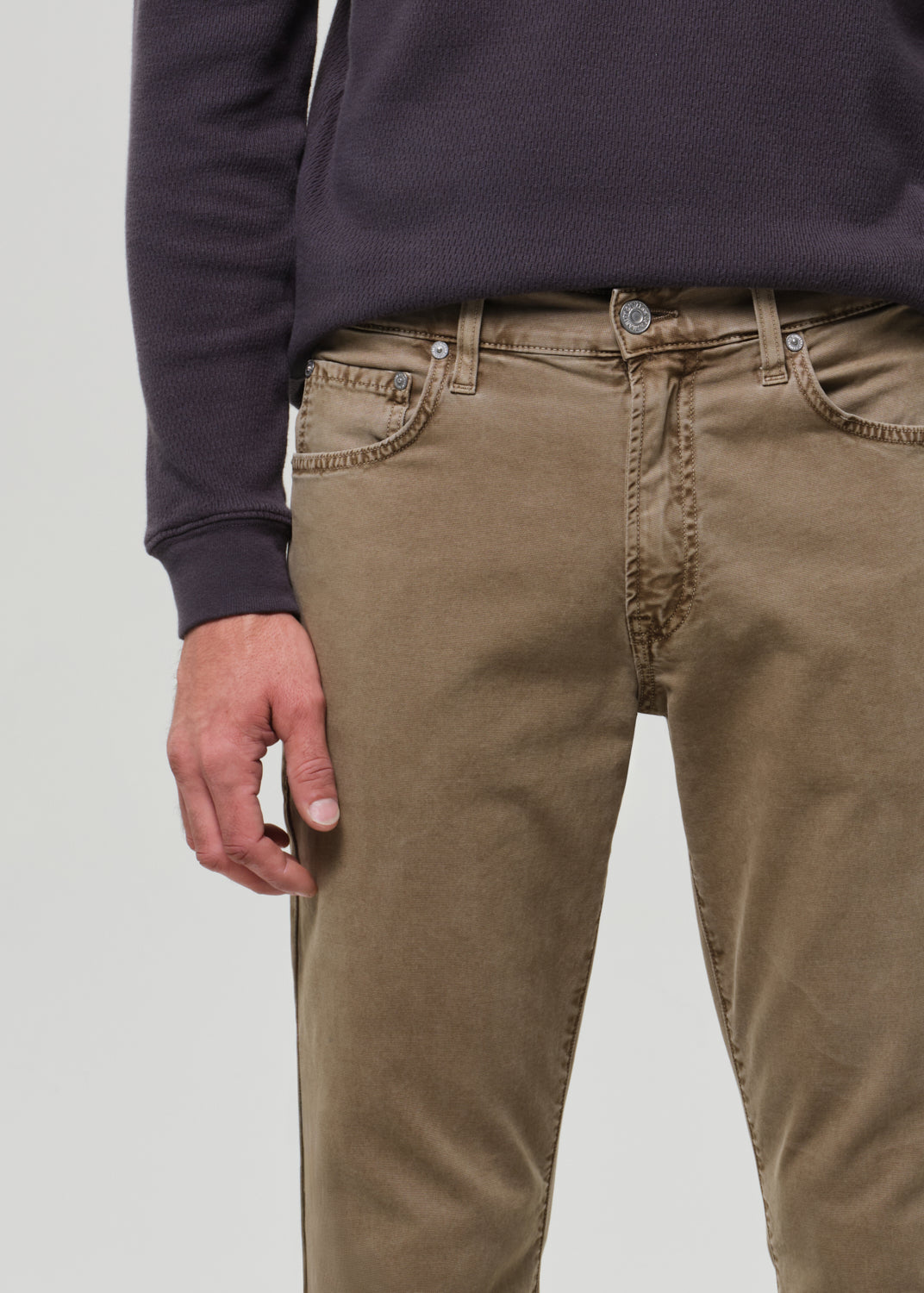 Person wearing a dark long-sleeve shirt and beige pants on a grey background