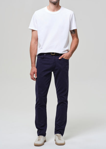 Man wearing a white t-shirt and navy pants on a plain background