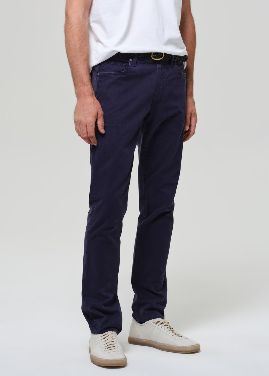 Man wearing a white t-shirt and navy pants on a plain background