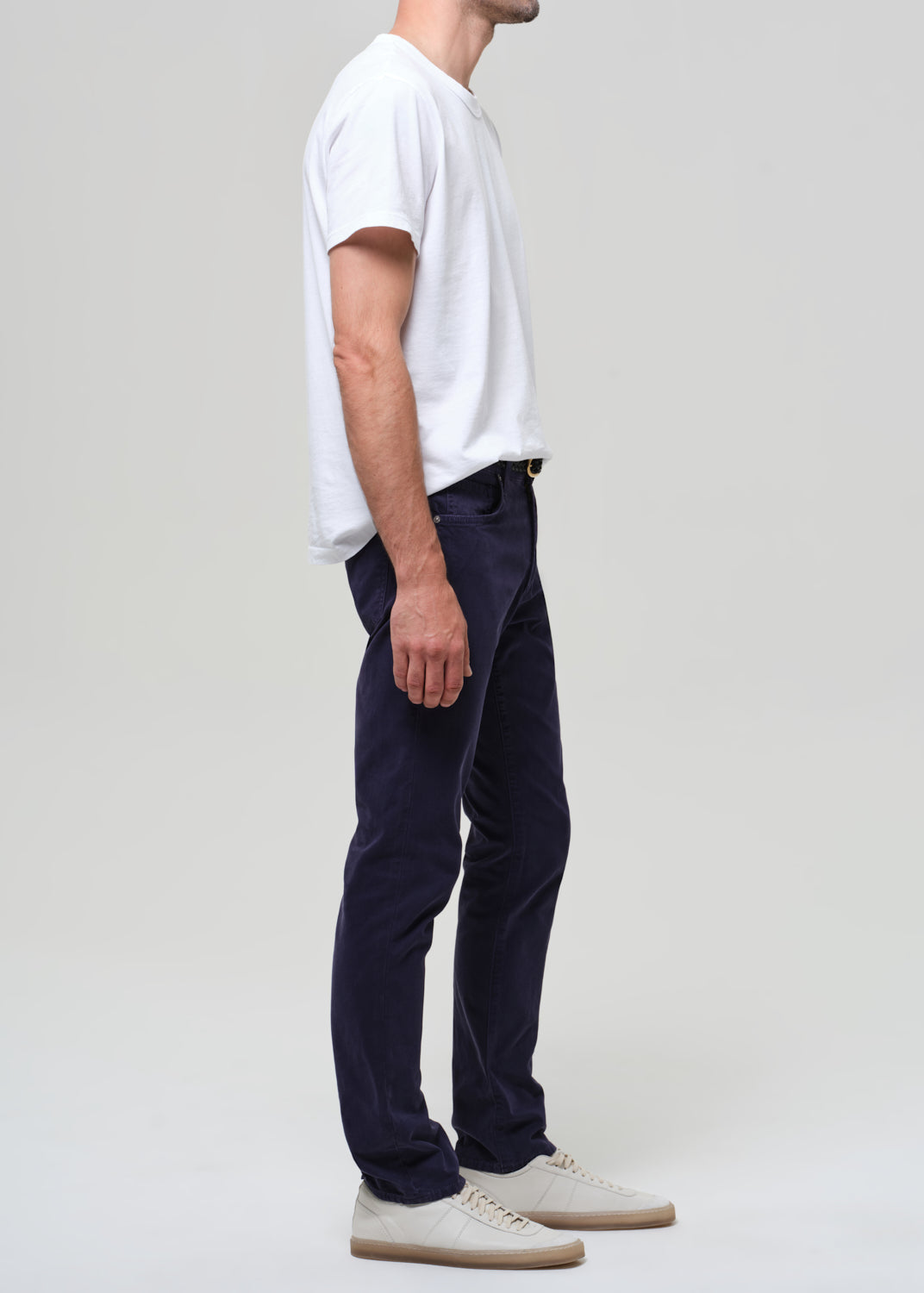 Man wearing a white t-shirt and navy pants on a plain background