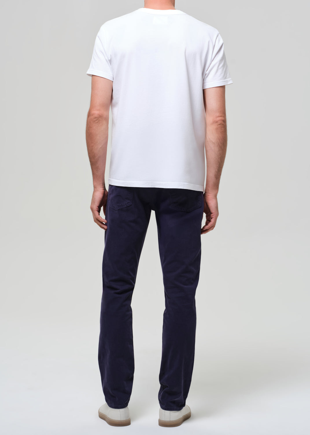 Man wearing a white t-shirt and navy pants on a plain background