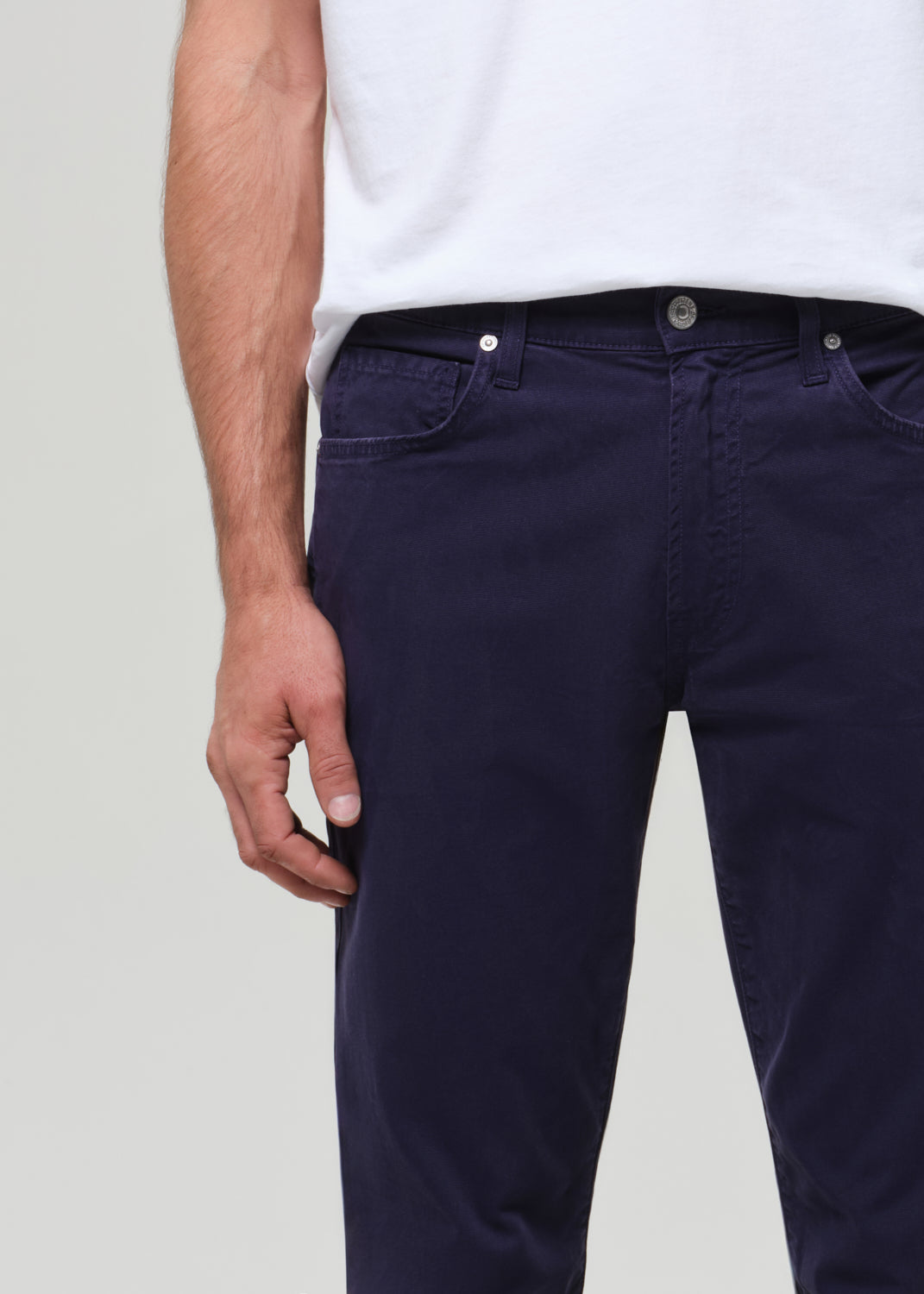 Man wearing a white t-shirt and navy pants on a plain background