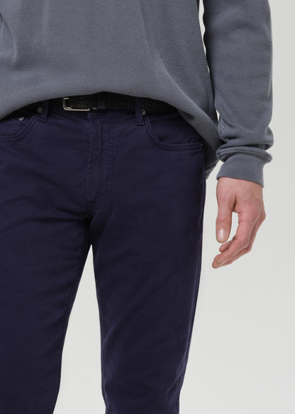 Close-up of a person wearing dark navy blue trousers and a grey ribbed long-sleeve top, cropped from the chest down against a grey background.