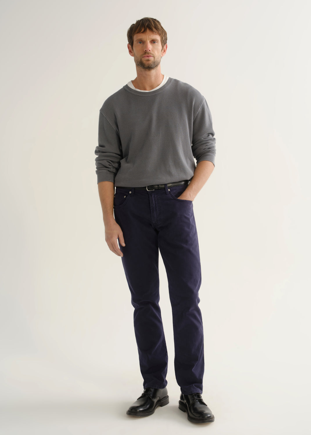 Person wearing a grey crewneck sweatshirt, dark navy pants, and black shoes, front full body view on a light grey background.
