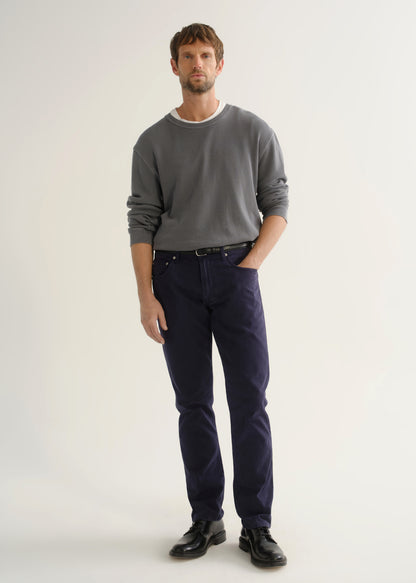 Person wearing a grey crewneck sweatshirt, dark navy pants, and black shoes, front full body view on a light grey background.