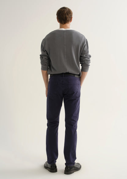 Person wearing a grey crewneck sweatshirt, dark navy pants, and black shoes, back full body view on a light grey background.