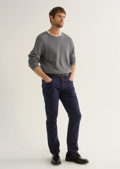 Person wearing a grey crewneck sweatshirt, dark navy pants, and black shoes, angled front full body view on a light grey background.
