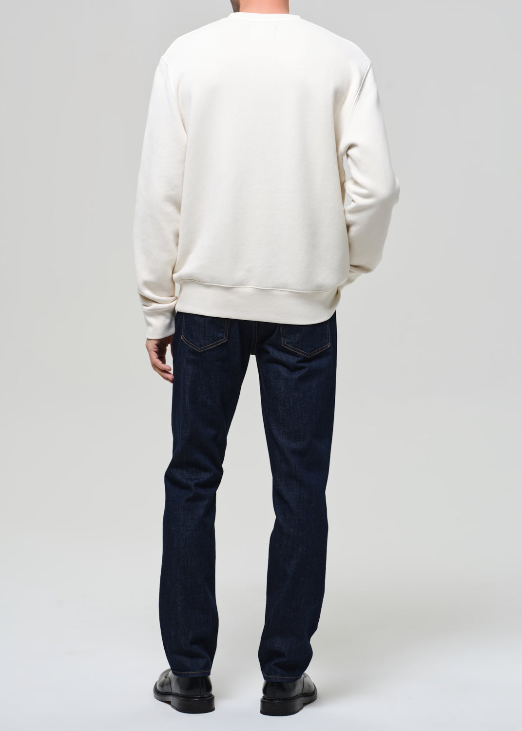 Person wearing a white sweatshirt and dark jeans on a plain background