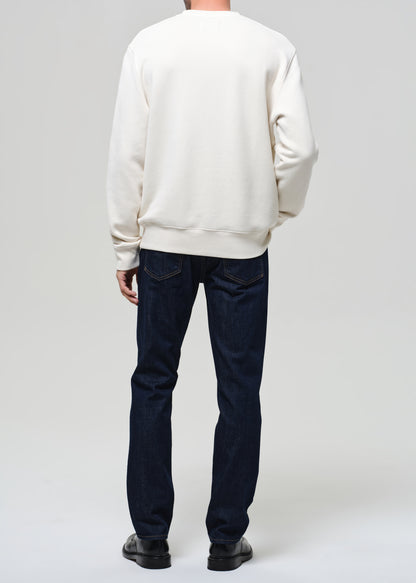 Person wearing a white sweatshirt and dark jeans on a plain background