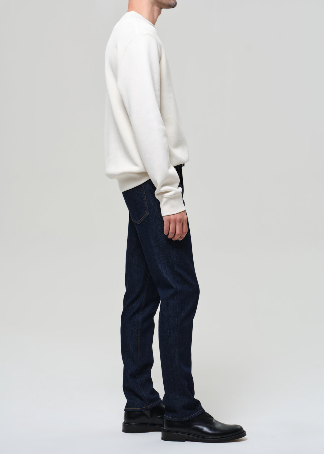 Person wearing a white sweater and dark blue pants on a plain background