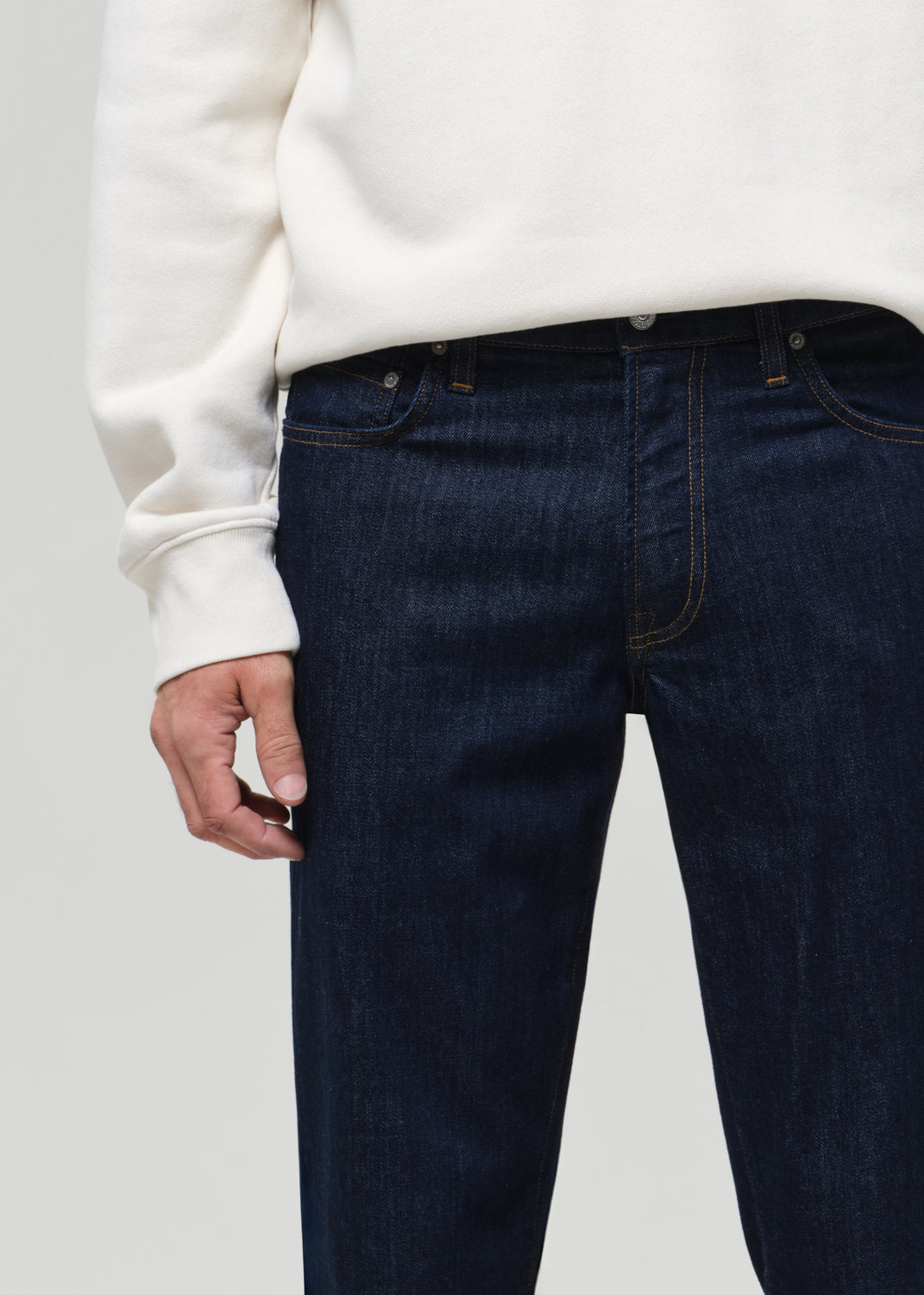 Person wearing dark blue jeans and a white sweatshirt on a plain background