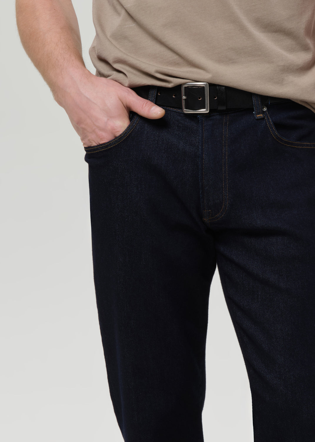Person wearing dark jeans and a beige shirt with a grey background