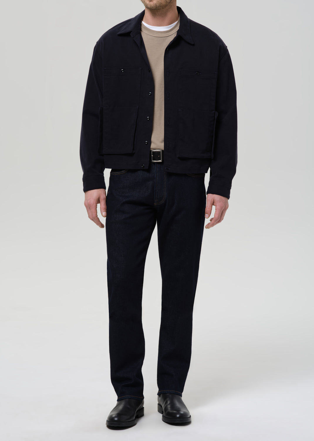 Person wearing a black jacket, beige shirt, and black pants on a grey background