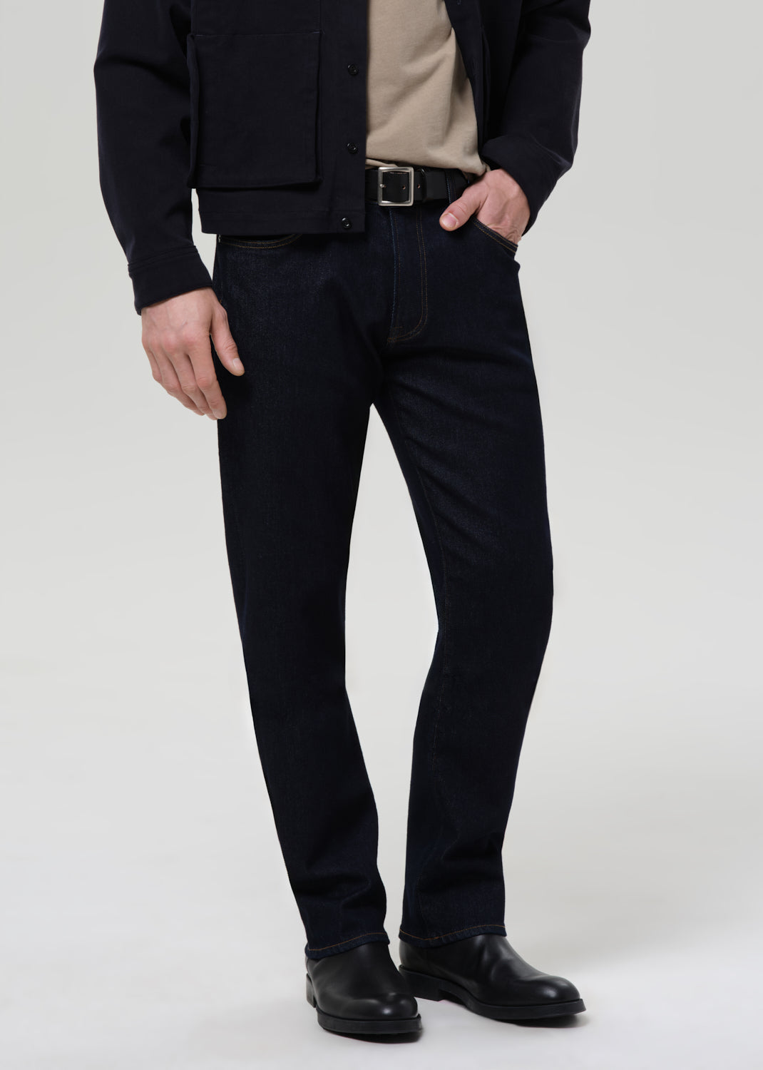 Person wearing black pants and a dark jacket on a grey background