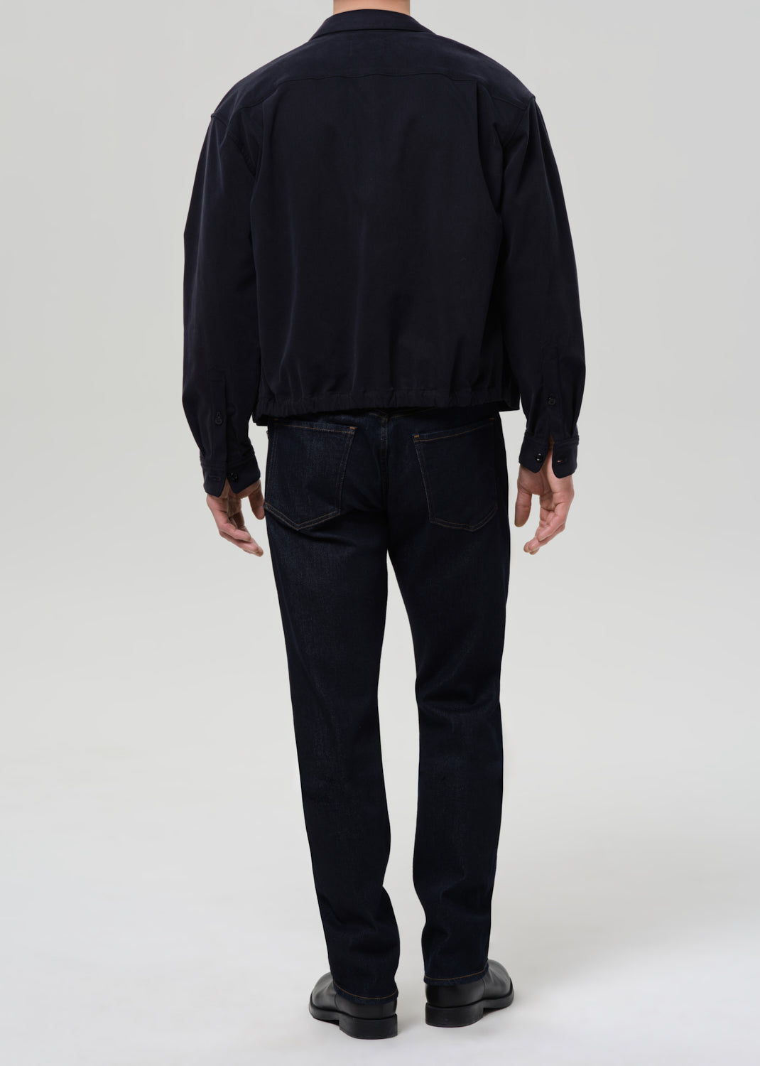 Person wearing a black jacket and pants on a grey background